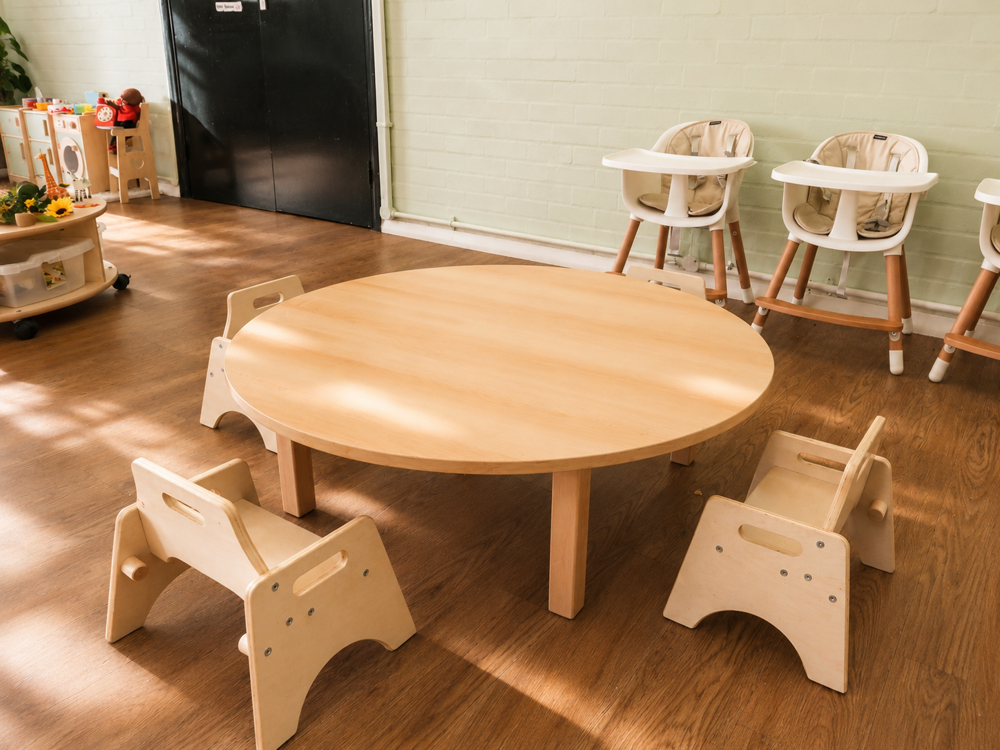 A natural wood round table with little chairs in a sunlit nursery room