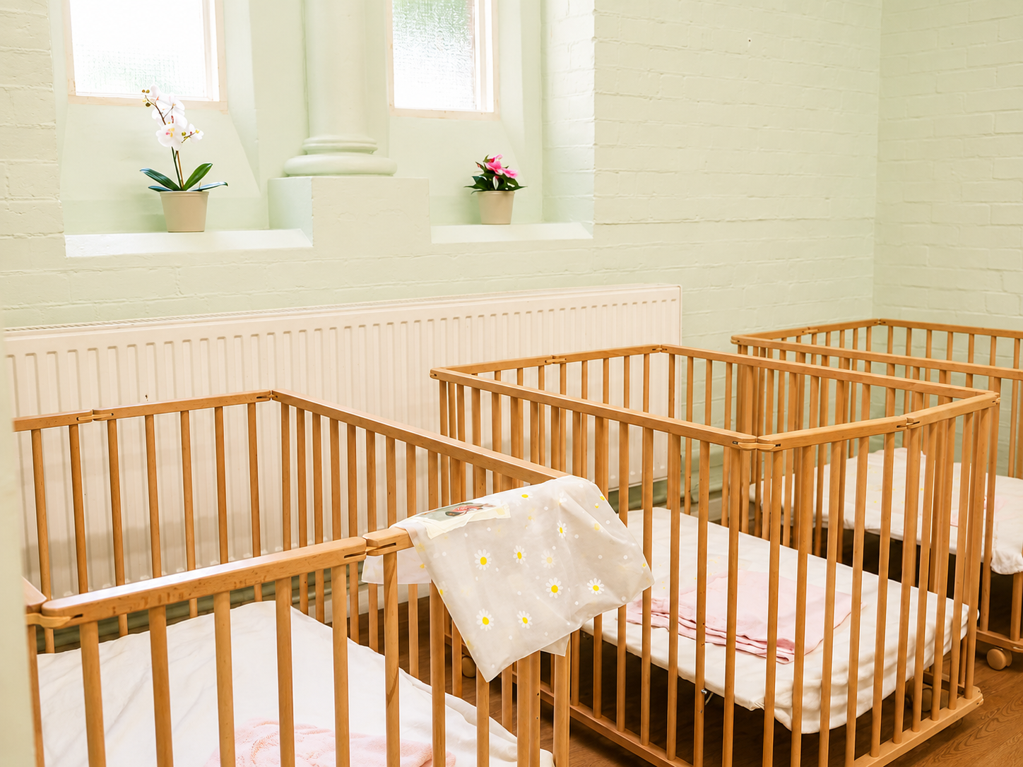 The calm, soft-green sleep room with wooden cots at Baby Grow Nursery